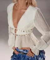 Blusa color crema de gasa con escote en V profundo, mangas largas abullonadas y detalle de monedas colgantes en el busto.