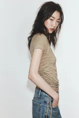 Camiseta corta de cuello redondo y manga corta, color gris oscuro, con frunces laterales ajustables mediante cordones.