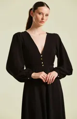 Vestido midi negro con escote en V profundo y botones dorados frontales. Presenta mangas largas abullonadas, corte en la cintura y falda fluida.
