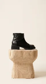 Bota corta de cuero negro con diseño de paneles que combina cuero liso, cuero con textura tipo reptil en el talón y gamuza en el lateral. Presenta cierre trasero, punta redondeada y taco geométrico bajo.