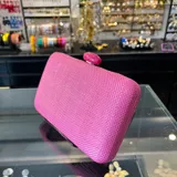 Clutch rectangular rígido de rafia sintética color fucsia, con cierre a tono y asa desmontable de cadena dorada para llevar al hombro.