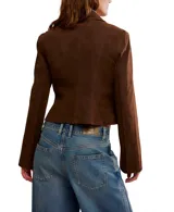 Chaqueta corta color marrón de gamuza vegana, con cuello clásico puntiagudo, cierre frontal y puños amplios.