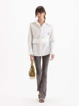 Camisa Oslo de poplín de algodón color blanco, con silueta estructurada, cuello camisero amplio, manga larga y cinturón ancho incorporado con hebilla rectangular forrada.