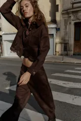 Chaqueta de cuello solapa y manga larga, color marrón oscuro, con efecto ante. Presenta bolsillos delanteros de plastrón, cierre frontal con botones y un bajo troquelado con diseño floral y acabado festoneado.