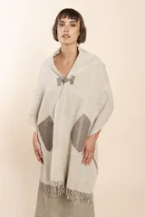 Chal de lana fina sin teñir con diseño de cuadros sutiles, cierre frontal con alamar y bolsillos de cuero metalizado. Presenta terminaciones con flecos en el ruedo y un calce estructurado en los hombros.