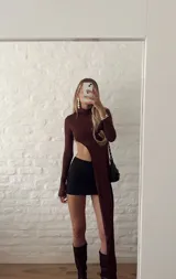 Top marrón de cuello alto y manga larga, con abertura en el abdomen y falda asimétrica.