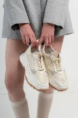 Championes chunky estilo tennis sneakers, color blanco y beige, con detalles en cuero y descarne. Incorporan un arnés desmontable con brillos y tachas, y suela de goma marrón.