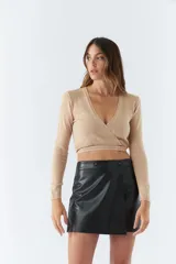 Top tejido de punto con diseño cruzado, escote en V y mangas largas. Cuenta con tiras para anudar en la cintura y detalle de grifa de cuero.