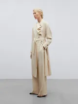 Vestido camisero midi color crema, de lino y viscosa, con cuello chal asimétrico, manga larga con puños abotonados, cierre frontal con botones y cinturón con hebilla forrada.