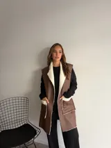 Chaleco largo de eco cuero color marrón con interior y detalles de corderito en solapas y bolsillos frontales.