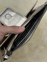 Billetera plateada con textura de piel de cocodrilo, cierre de cremallera y correa de muñeca.