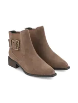 Botín chelsea de cuero gamuza color marrón taupe, con taco intermedio símil madera y detalle de hebilla metálica ornamental en el lateral.