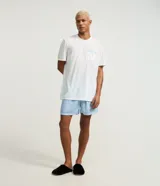 Conjunto de pijama corto para hombre, compuesto por una remera blanca de manga corta, cuello redondo y un bolsillo en el pecho con detalle a rayas, y un short celeste con estampado de rayas finas y cintura elástica.