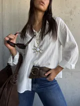 Camisa blanca de corte clásico con textura de rayas verticales sutiles, cuello camisero, cierre frontal de botones y mangas largas con puños.