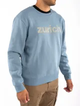 Sudadera celeste con cuello redondo, puños y cintura acanalados. Estampado frontal con la palabra "Zurich" en letras plateadas.