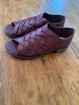 Sandalias de cuero bordó con diseño de tiras cruzadas y entrelazadas en la parte frontal, talón cerrado y suela plana de goma.