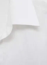 Camisa blanca de lino de corte regular y diseño recto, con cuello camisero, cierre frontal de botones ocultos y mangas largas con puños abotonados.
