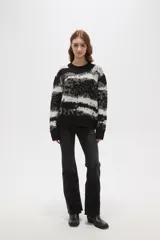Sweater de tejido jacquard con diseño de rayas irregulares en tonos negro, blanco y gris. Presenta cuello redondo a la base, mangas largas y un corte holgado.