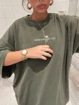 Remera oversize de color marrón topo con efecto acid wash, cuello redondo y manga corta. Cuenta con un pequeño estampado gráfico frontal con el texto 'WAKE UP IND' y una calavera.