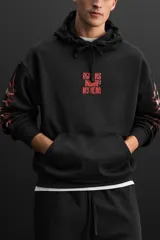 Buzo hoodie negro oversize con estampado rojo en el pecho y diseño tribal en las mangas.