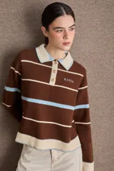 Buzo tipo polo de tejido de punto, color marrón con rayas horizontales en celeste y crema. Presenta cuello camisero, cierre frontal con tres botones y logo bordado en el pecho.