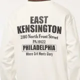 Buzo de felpa color blanco hueso, con cuello redondo y puños y ruedo acanalados. Presenta una pequeña impresión en el pecho con texto que incluye "EAST KENSINGTON PHILADELPHIA".