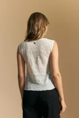 Top sin mangas de jacquard color negro, con cuello cerrado y silueta recta. Presenta una textura trabajada con relieve y una terminación suavemente ondulada en el ruedo.