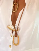 Collar con dije ovalado de bronce colgando de un tiento de cuero marrón.