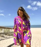 Vestido camisero de corte oversize con estampado de hojas tropicales en colores violeta, fucsia y verde. Presenta cuello mao, cierre frontal con botones y mangas cortas holgadas.