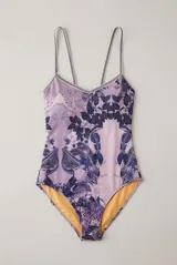 Malla enteriza de diseño simétrico con estampado de fauna y follaje en tonos lilas y azules, tirantes dobles finos y ribetes decorativos.