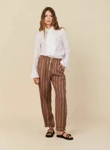 Pantalón babucha de lino a rayas verticales marrones y blancas, con cinturilla elástica con lazo para anudar y tres bolsillos funcionales.