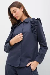 Camisa de gabardina de tencel color negro, con cuello clásico, cierre frontal de botones y volados fruncidos en los hombros.