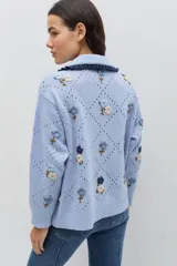 Saco de punto color bordó con bordados artesanales de flores en tonos rosados. Presenta un cuello con detalle de volados en color crema y cierre frontal con botones. De silueta amplia y cómoda.