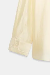 Camisa de mujer fluida de ZARA WOMAN COLLECTION, confeccionada en hilatura con mezcla de lyocell. Presenta escote en pico, manga larga con puños marcados y bajo asimétrico, con cierre frontal de botones ocultos.