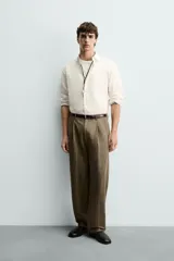 Pantalón de corte relajado confeccionado en mezcla de algodón y lino, con diseño de pliegues frontales, bolsillos laterales y bolsillos traseros de vivo. Presenta cierre frontal con cremallera y botón, con un acabado de lavado especial que le otorga una apariencia única.