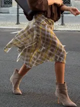 Falda midi asimétrica con estampado de cuadros en tonos amarillos, grises y blancos. Confeccionada en tela fina y semitransparente con caída fluida.