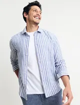 Camisa de lino a rayas verticales azules y blancas, de manga larga con cuello clásico y cierre con botones.