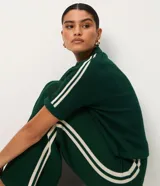 Blusa femenina de punto color verde oscuro, con cuello polo y abertura delantera sin botones. Presenta una trama ahuecada con textura uniforme y mangas cortas con detalle de rayas blancas en los hombros. El modelo es recto y de largo regular.