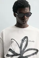 Camiseta de corte relajado confeccionada en algodón, con cuello redondo y manga corta. Presenta un estampado artístico de una flor a trazo grueso en color negro sobre fondo blanco.