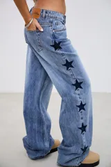 Pantalón de jean tiro medio con corte recto y holgado, presenta bordados de estrellas oscuras a lo largo de los laterales externos.