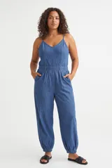 Mono enterito de denim en color azul claro, con tirantes finos, escote en V y bolsillos laterales. Las botamangas cuentan con elástico fruncido.