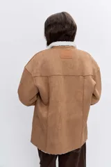 Cazadora de efecto piel en color tostado con interior y solapas de borreguillo blanco. Presenta cierre frontal con botones, bolsillos laterales y mangas largas con puños de borreguillo.