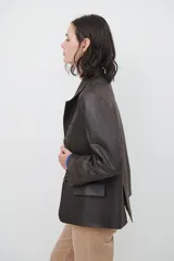 Blazer de cuero color marrón, con corte entallado, cuello con solapas, cierre frontal con botones y bolsillos laterales con solapa.