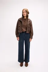 Campera corta de cuero sintético en color marrón, con diseño de calce relajado, cierre frontal metálico, bolsillos laterales con solapa y botones a presión, y cuello camisero.