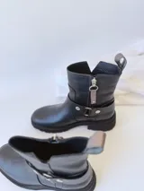 Bota corta negra de cuero, con caña media, hebilla lateral y suela track.