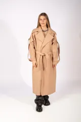 Tapado largo de paño color beige, con solapas amplias, cierre frontal cruzado con cinturón ajustable y detalles de tiras decorativas en las mangas.