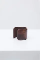 Pulsera rígida tipo brazalete de cuero en color crudo con textura efecto cocodrilo y costuras decorativas en los bordes.