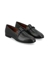 Mocasín de cuero color negro, de estilo sastrero, con costuras visibles alrededor de la puntera y detalle de hebilla forrada en el empeine.
