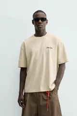 Camiseta relaxed fit color beige, con cuello redondo y manga corta. Presenta un bordado y estampado combinado a contraste en el delantero y la espalda.