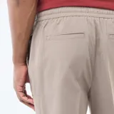 Pantalón de corte jogger en color beige, confeccionado con cintura elástica ajustable mediante cordón y bolsillos laterales.